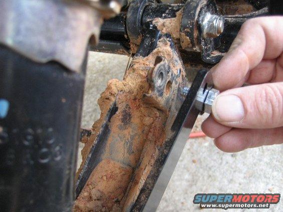 ATV suspension part covered in mud, with a hand tightening a bolt