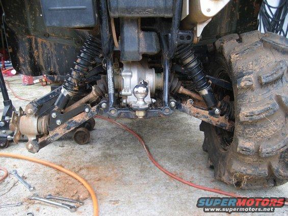 ATV rear suspension with large mud tires, hitch ball, and tools on concrete