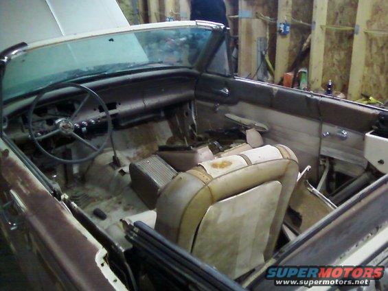 Interior view of a vintage convertible car with worn seats and dashboard, undergoing restoration