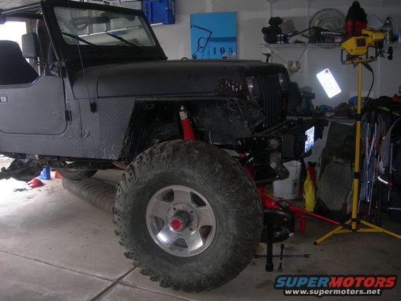 Black Jeep Wrangler with large tires and red shocks, parked in a garage