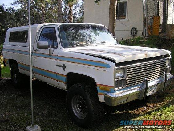White pickup truck with blue and orange stripes and a camper shell. Hood is open
