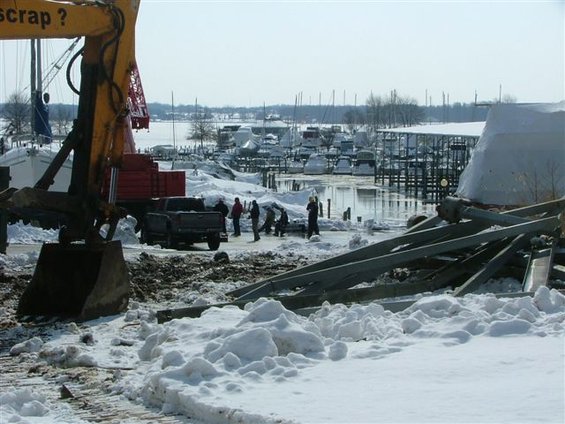 Excavator and pickup truck at a snowy marina with boats docked