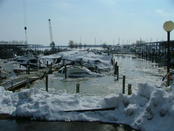 Boats covered in snow and ice in a frozen marina with cranes visible