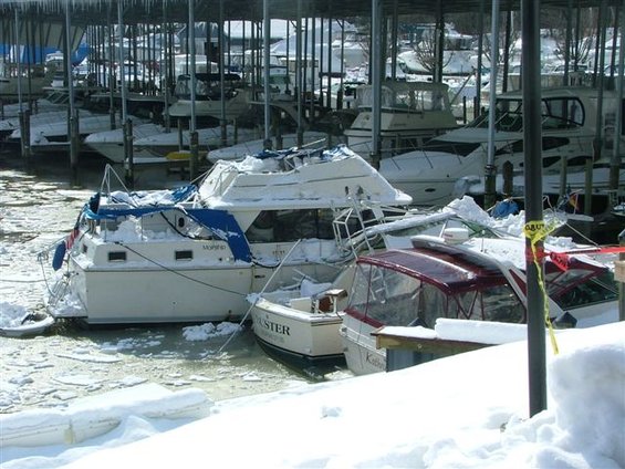 Boats covered in snow and ice docked under a shelter in winter