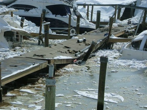 Damaged marina dock covered in snow, with several boats partially visible