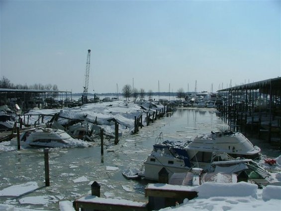 Boats covered in snow and ice at a marina, with a crane in the background
