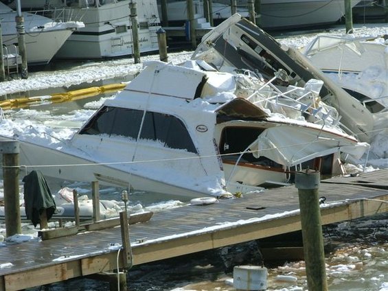 Damaged white boats covered in snow and ice at a dock