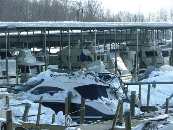 Boats covered in snow under a covered dock, one boat appears damaged