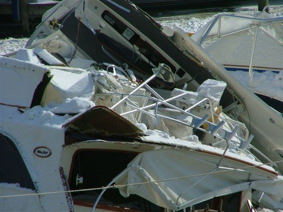 Wrecked white boats covered in snow, with a steering wheel visible