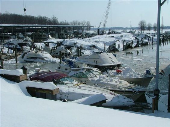 Boats covered in snow and ice at a marina, with some docks damaged