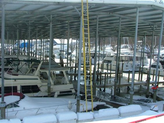 Boats covered in snow docked under a metal canopy at a marina
