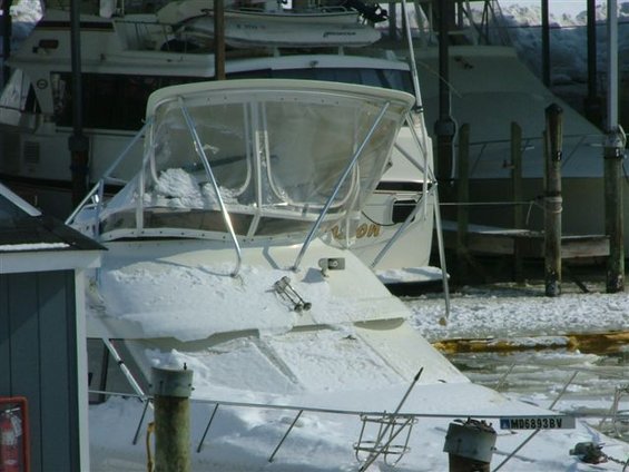 Boat covered in snow at a marina with other boats docked