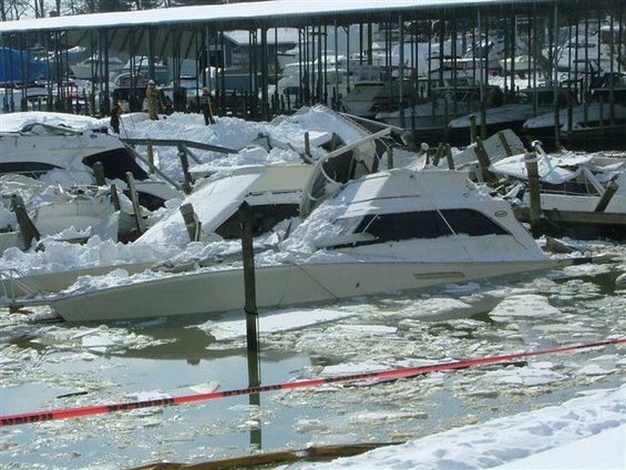 Boats piled up and partially submerged in icy water with snow covering everything