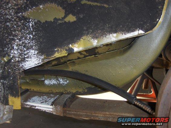 Underside view of a vehicle's frame rail and suspension components, with a black hose visible