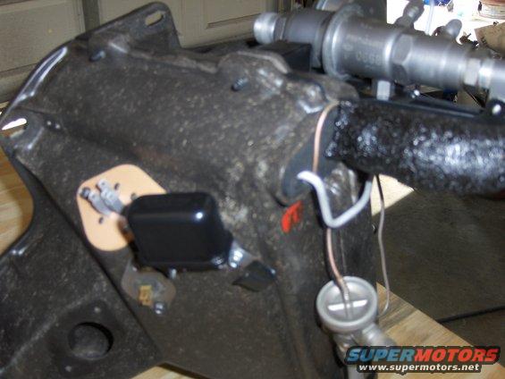 Black plastic component attached to a dark, textured metal housing with wires and a silver fitting