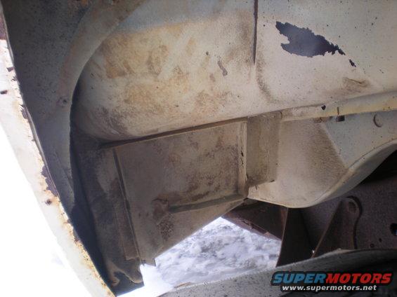 Undercarriage of a vehicle with rust and dirt, showing frame components and suspension parts