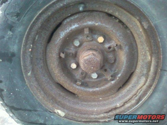 Rusted wheel hub with lug nuts and part of a tire