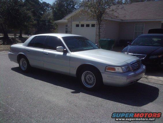Silver sedan parked on a street, front passenger side visible. Tinted windows, wire-spoke wheels