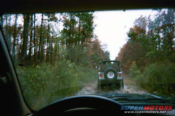 Driving behind a Jeep Wrangler on a muddy trail through trees