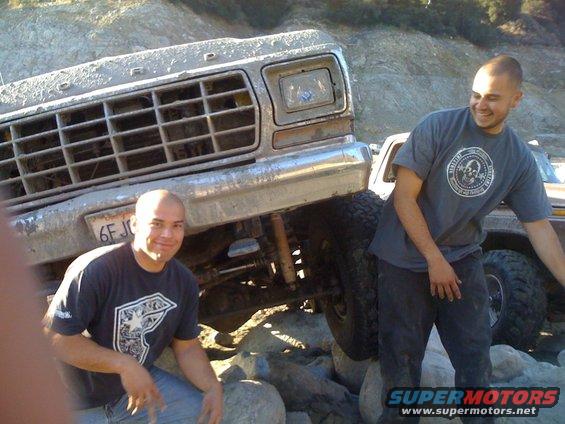 Mud-covered 1973 Ford F-Series truck front grille and bumper, with two men standing nearby