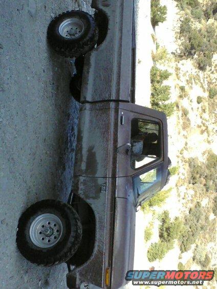 Brown Ford F-250 pickup truck parked on a dirt road with a wooded hillside in the background