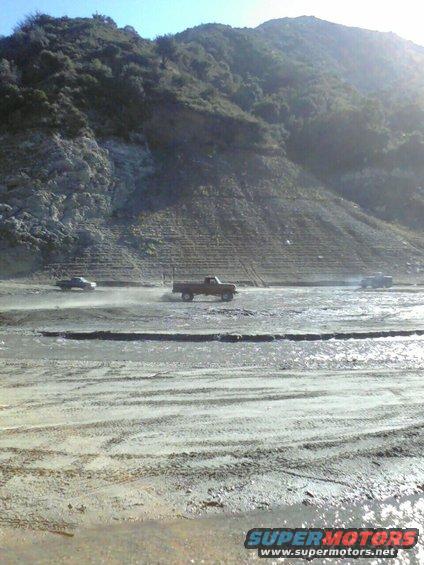 Brown 1973 Ford F-250 driving on a muddy road with a hill in the background