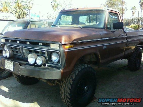 Brown 1973 Ford F-250 pickup truck with aftermarket lights and large tires, parked next to another vehicle