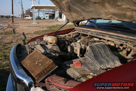 Engine bay of a red truck with hood open, air filter removed