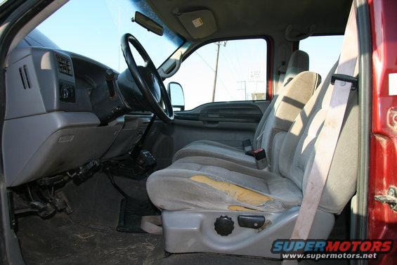 Interior of a red truck showing the driver's seat, dashboard, and steering wheel. The driver's seat has torn upholstery