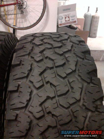 Close-up of aggressive off-road tire tread. A bicycle wheel is visible in the background