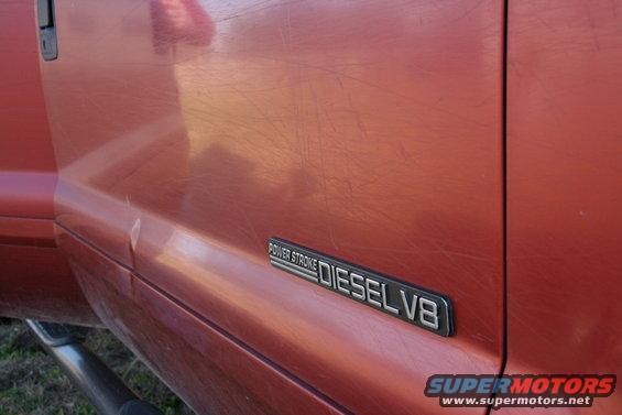 Close-up of a red Ford truck door with a 'POWER STROKE DIESEL V8' badge. Scratches are visible on the paint