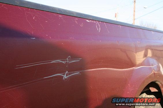 Red truck side panel with numerous scratches and white pinstripes