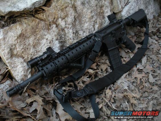 Black rifle with sling and tactical light resting on rocks and leaves