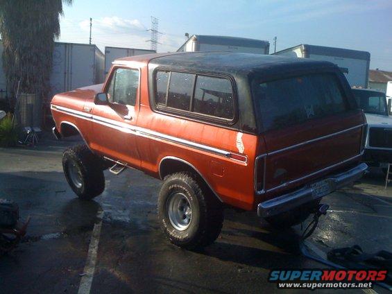Orange 1978 Ford Bronco with a black top, lifted on large tires, viewed from the rear-right