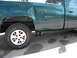 1995 GMC Sierra 1500 - Rear quarter panel and wheel of a green 1995 GMC Sierra 1500 pickup truck with a dent.