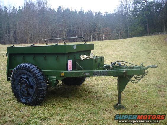 Green military trailer with large tires parked on a grassy field