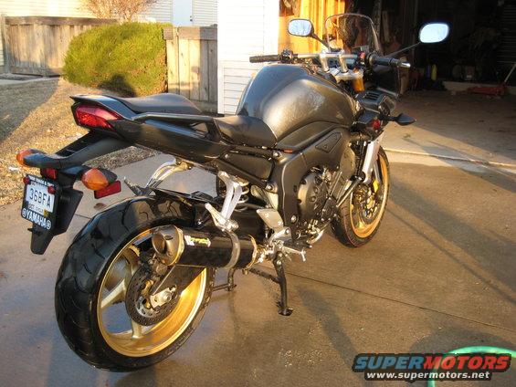 Black motorcycle with gold wheels and aftermarket exhaust, rear view
