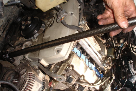 Engine bay with a hand holding a carbon fiber tool over the engine