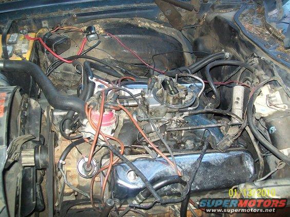 Engine bay with carburetor, distributor, and battery visible. Wires and hoses are messy