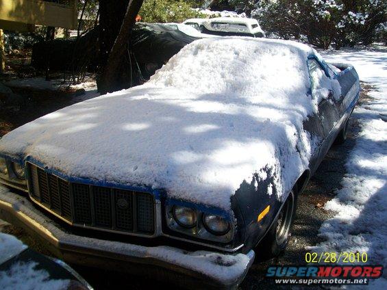 Dark blue Ford Ranchero covered in snow, front 3/4 view. Grille and headlights visible