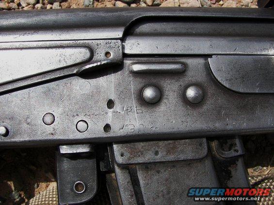 Close-up of a metallic firearm receiver with stamped markings and rivets