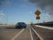 1983 Mercury Capri - A blue hatchback drives on a highway towards a dead end sign.