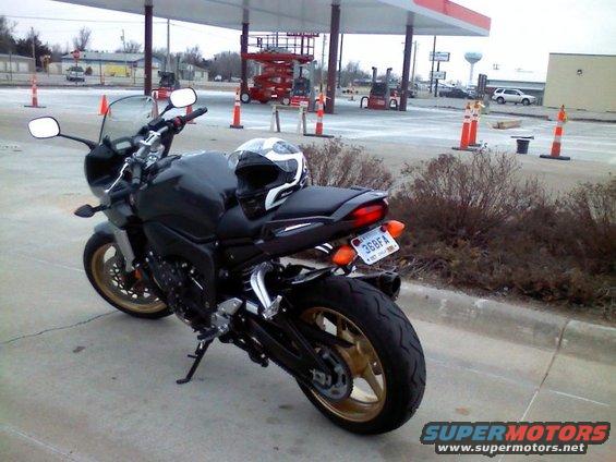 Black motorcycle with gold wheels parked at a gas station, helmet on seat