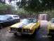1973 Mercury Cougar - A yellow 1973 Mercury Cougar convertible is parked next to another yellow car and a dark pickup truck with a camper shell.