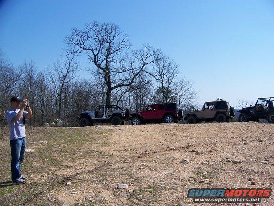 Four Jeeps parked on a dirt hill with a man taking a photo