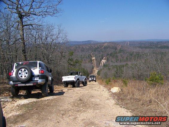 Silver SUV, white convertible SUV, and black SUV on a dirt road in a wooded area