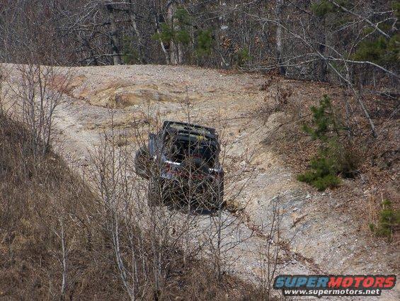 Off-road vehicle driving up a steep, rocky dirt path surrounded by trees
