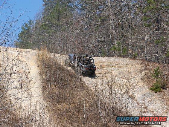 Dark off-road vehicle with roll cage climbing a dirt hill, rear view