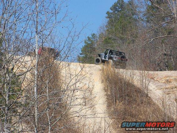 Gray Jeep Wrangler climbing a dirt hill, another vehicle behind