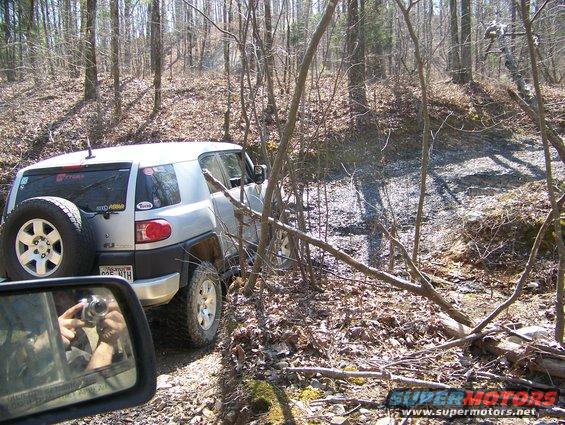 Silver Toyota FJ Cruiser on a dirt trail in the woods, spare tire mounted on rear door